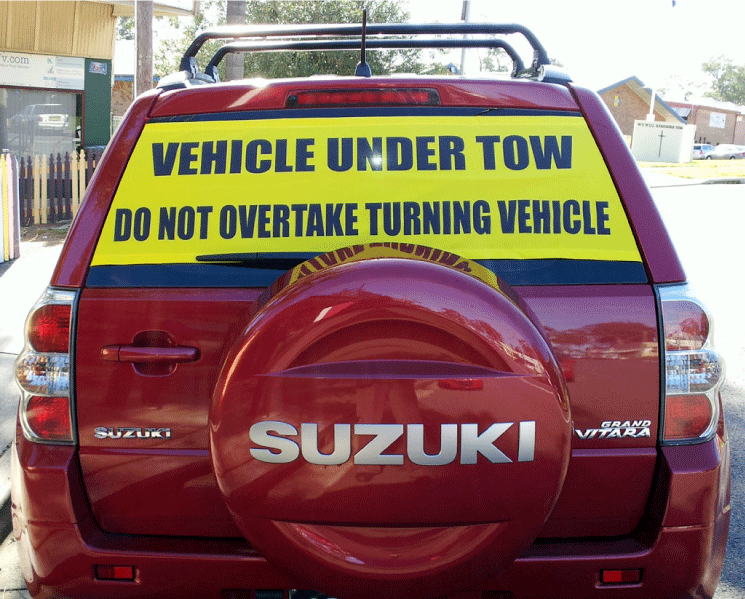 Tow Smart Regular sign on the outside of a Suzuki Grand Vitara rear window: Vehicle Under Tow